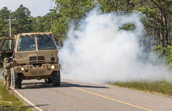 A large tan colored Army vehicle rounding a turn on a dirt road in the training area. 